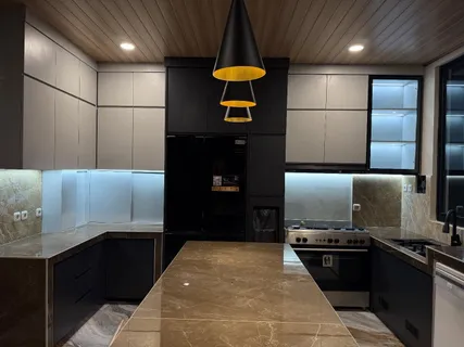 Kitchen set hitam dan abu dengan island panjang, plafon kayu, dan lampu gantung