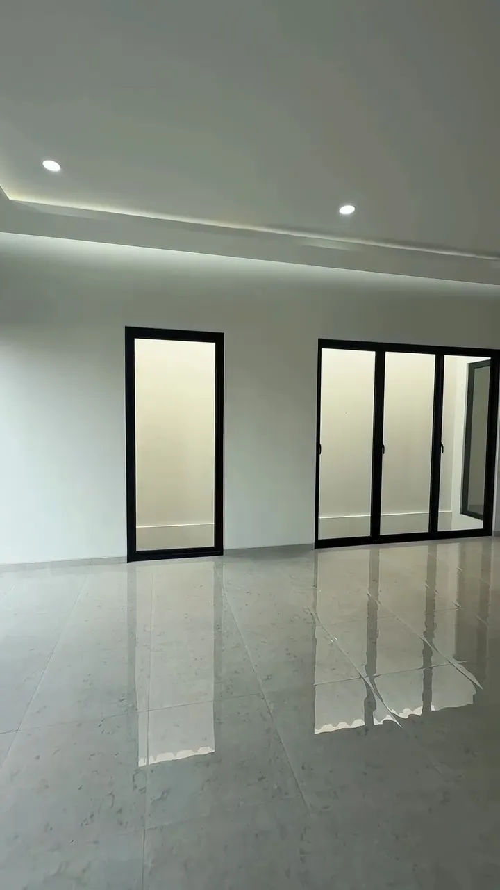 Ruang keluarga kosong dengan lantai granit mengilap dan pintu kaca berkusen hitam