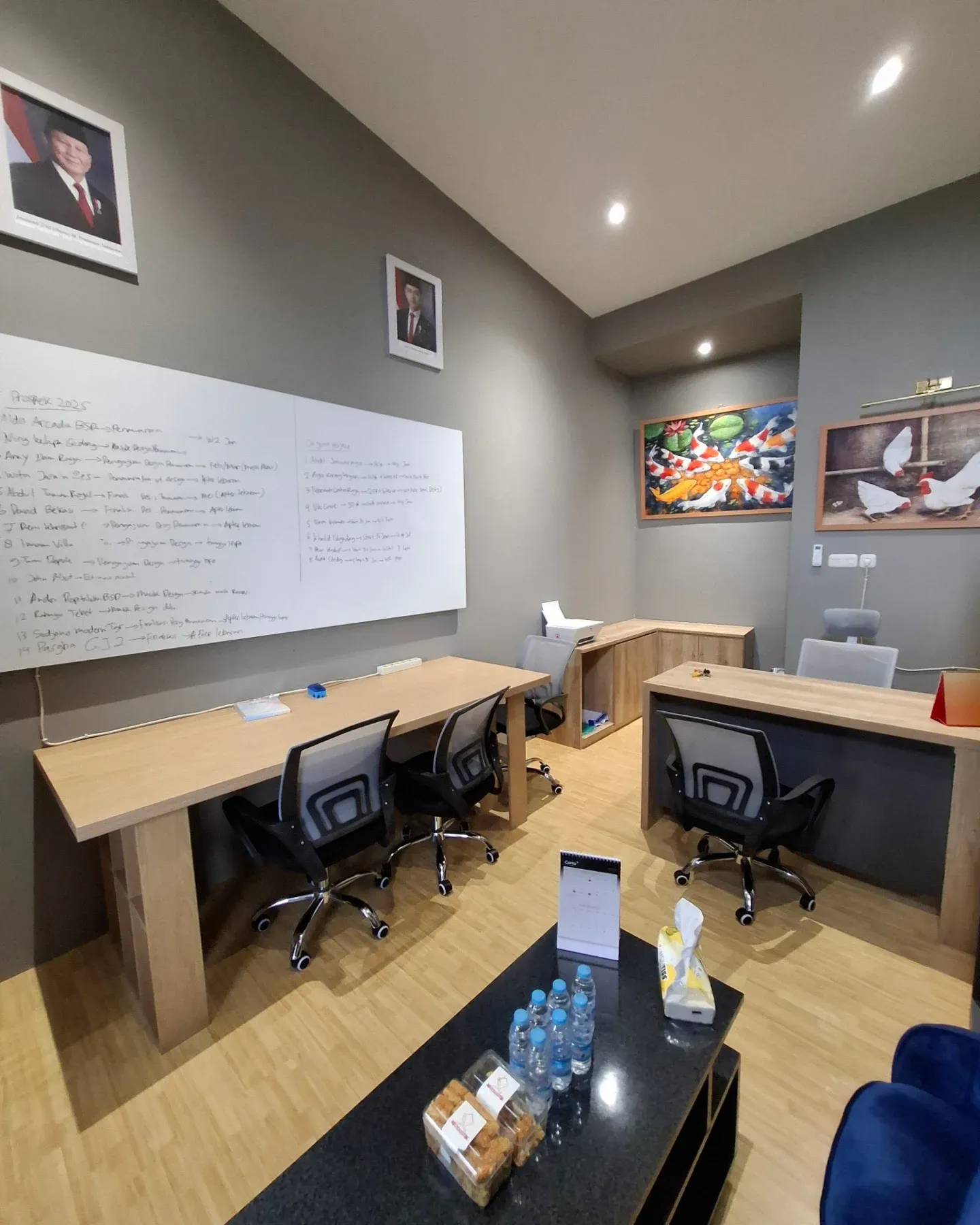 Ruang kerja kantor dengan meja kayu memanjang, kursi kerja hitam, dan papan tulis di dinding