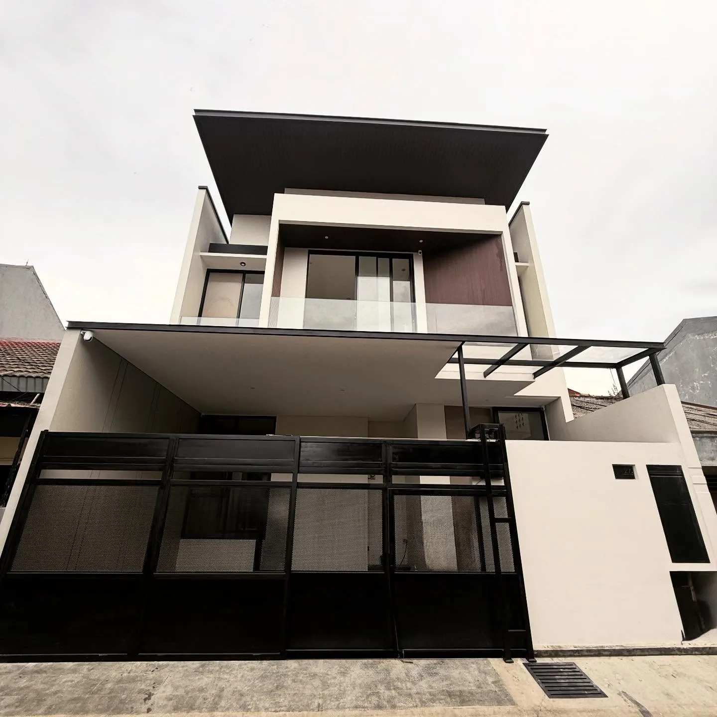 Rumah modern kontemporer tiga lantai dengan atap datar menjorok dan pagar besi hitam