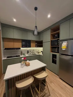 Kitchen set sage green dengan island terrazzo, dua kursi bar kayu, dan lampu gantung hitam