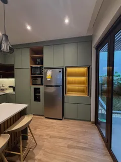 Kabinet tinggi sage green dengan kulkas tanam dan rak pajangan berlampu hangat