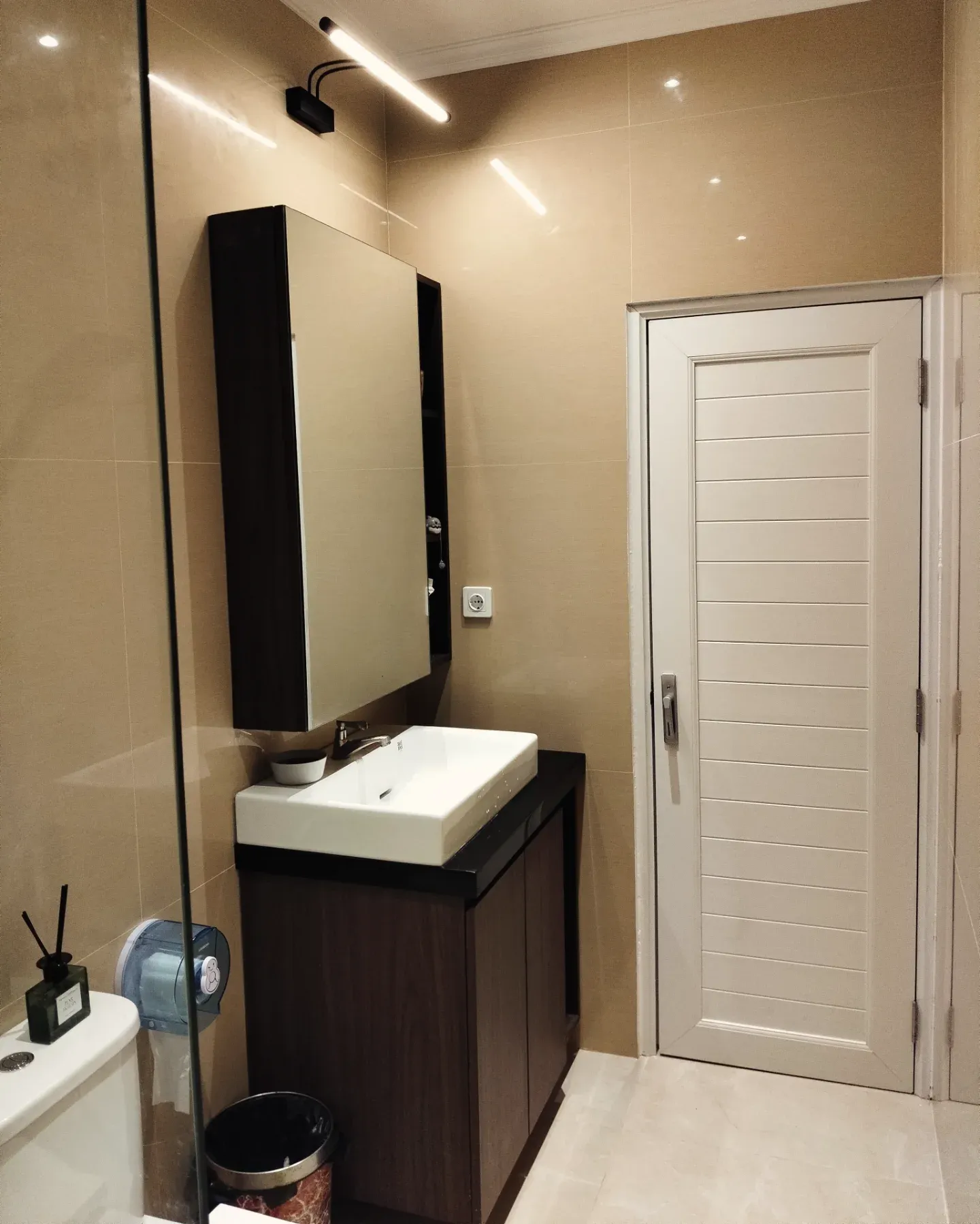 Kabinet wastafel melayang warna gelap dengan lemari cermin di kamar mandi krem