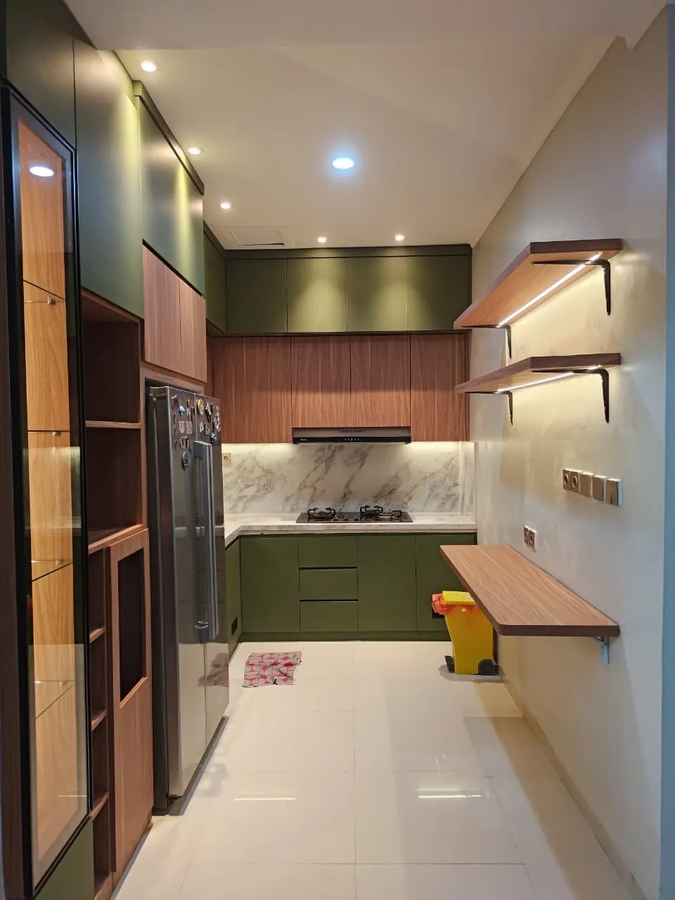 Dapur memanjang dengan kabinet hijau, backsplash marmer, dan ambalan kayu berlampu LED